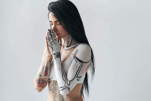 A woman with her hands clasped wearing makeup that looks like a robot arm in white and black.