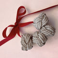 Three knotted gray rope ornaments tied to a red ribbon, arranged on a light pink background.