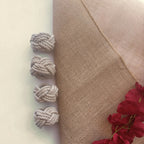 Four knotted gray rope tassels arranged vertically on the left side of a beige fabric panel, next to a white background and red flowers in the bottom right corner.