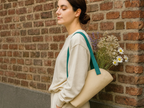 Woman holding a beige tote bag with flowers against a brick wall