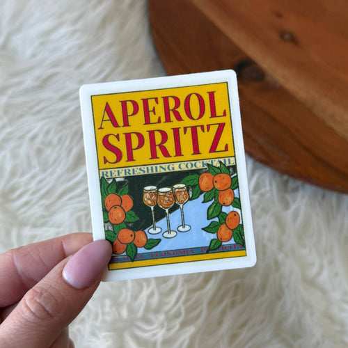 Card with Aperol Spritz branding held by a hand on a textured surface