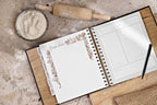 Open planner with decorative elements on a kitchen counter with flour and rolling pin.