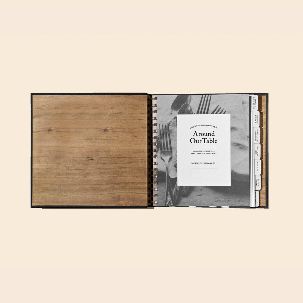 Open spiral-bound notebook with wooden cover and 'Around Our Table' branding on a beige background