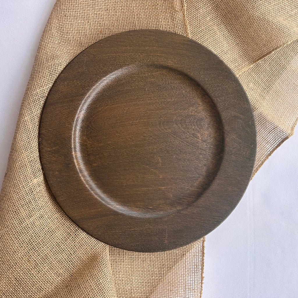 A round dark brown wooden tray with a raised rim, shown from above on a beige burlap fabric background.