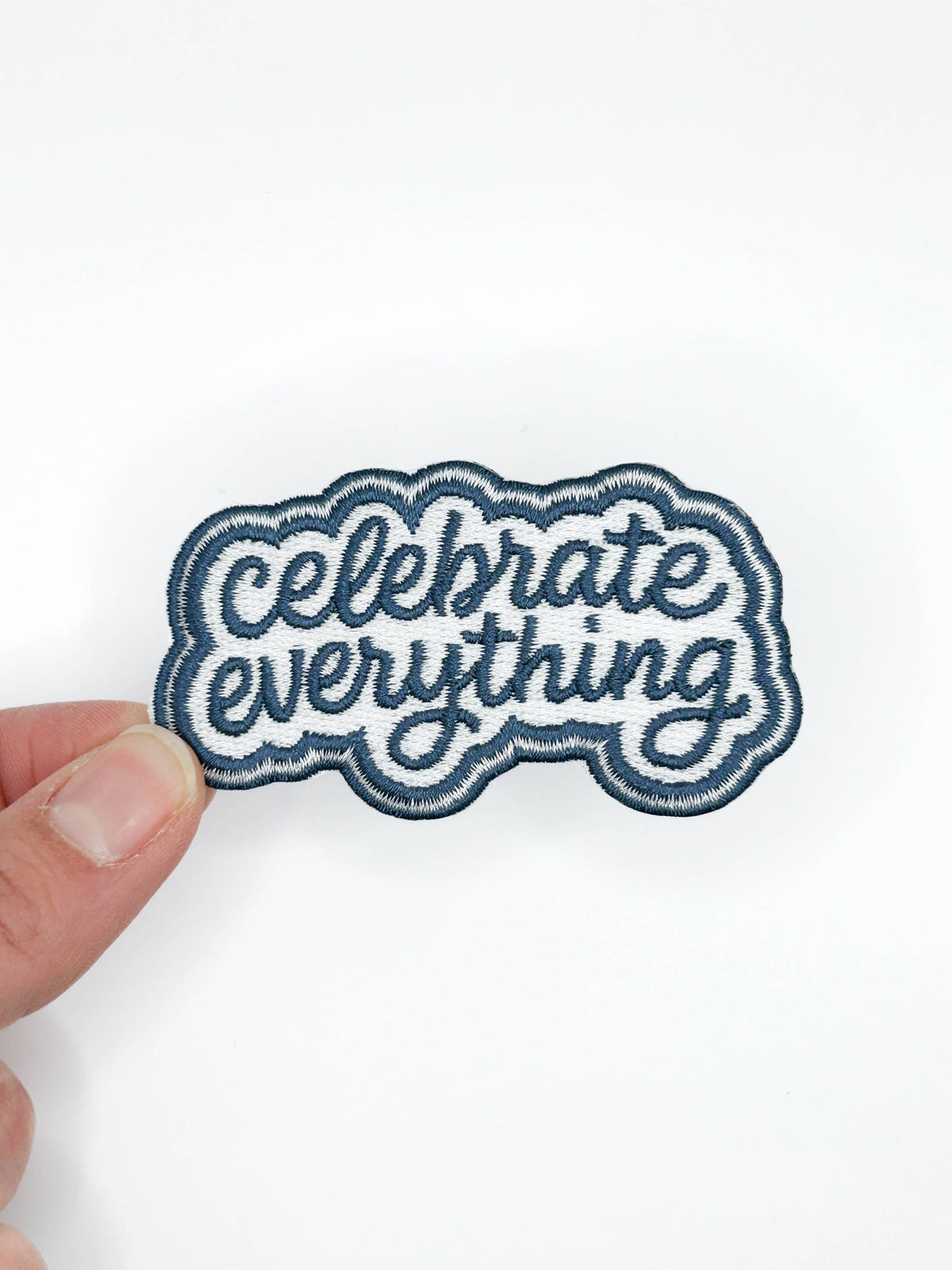 Patch with 'Celebrate Everything' text held by a hand on a white background