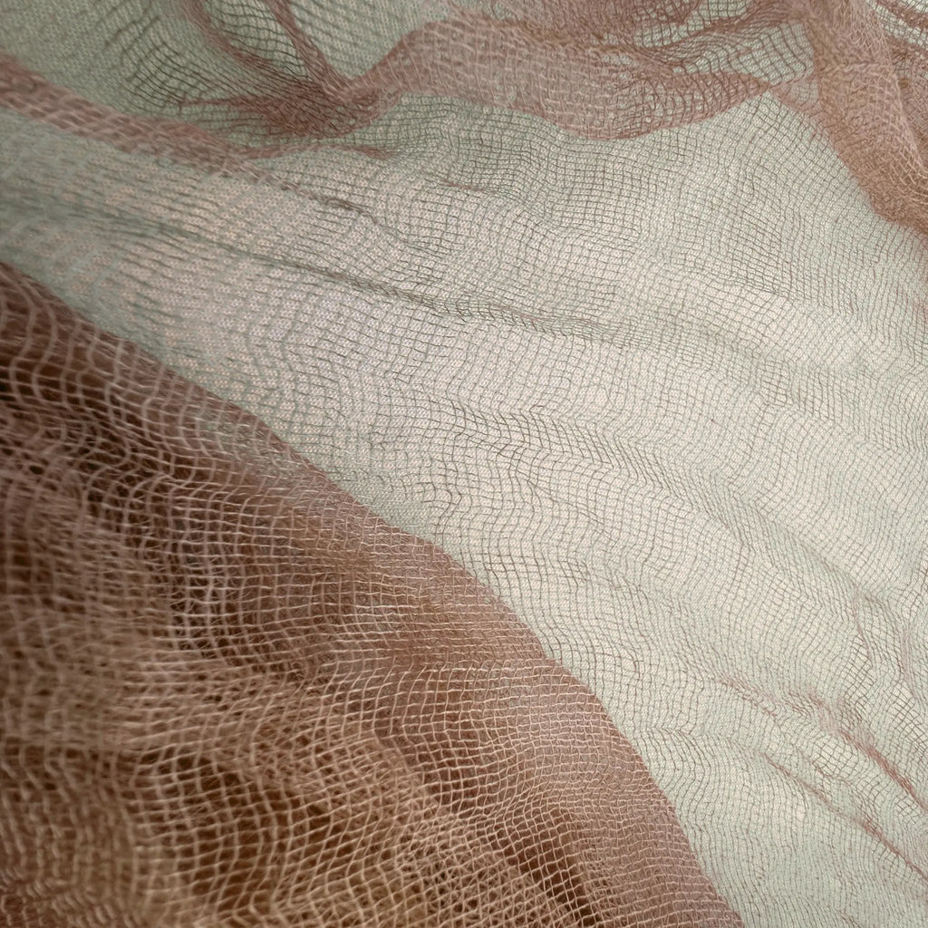 A close-up of sheer mesh fabric with a fine grid texture, layered in soft blush pink and warm taupe-beige tones.