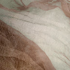 A close-up of sheer mesh fabric with a fine grid texture, layered in soft blush pink and warm taupe-beige tones.