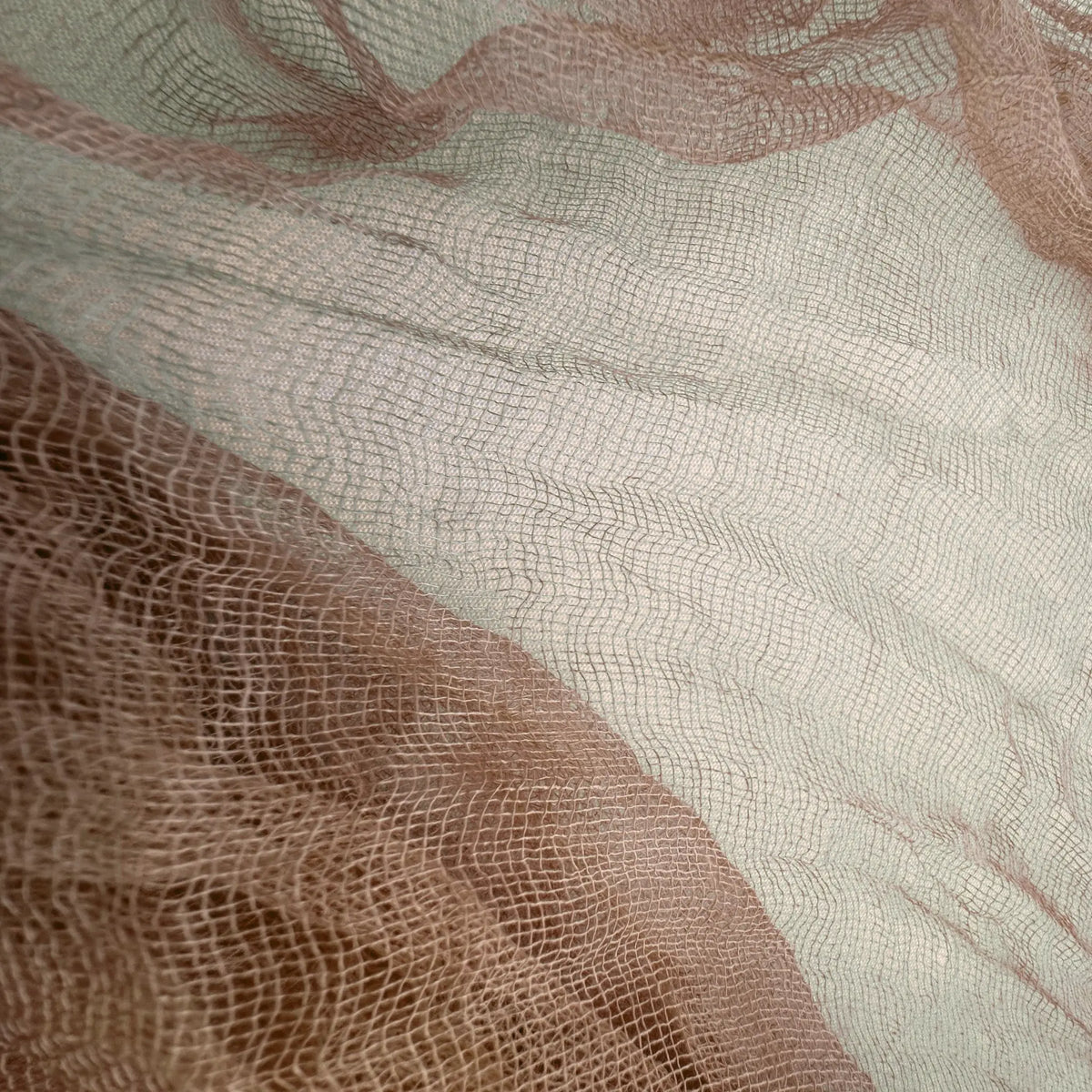 A close-up of sheer mesh fabric with a fine grid texture, layered in soft blush pink and warm taupe-beige tones.