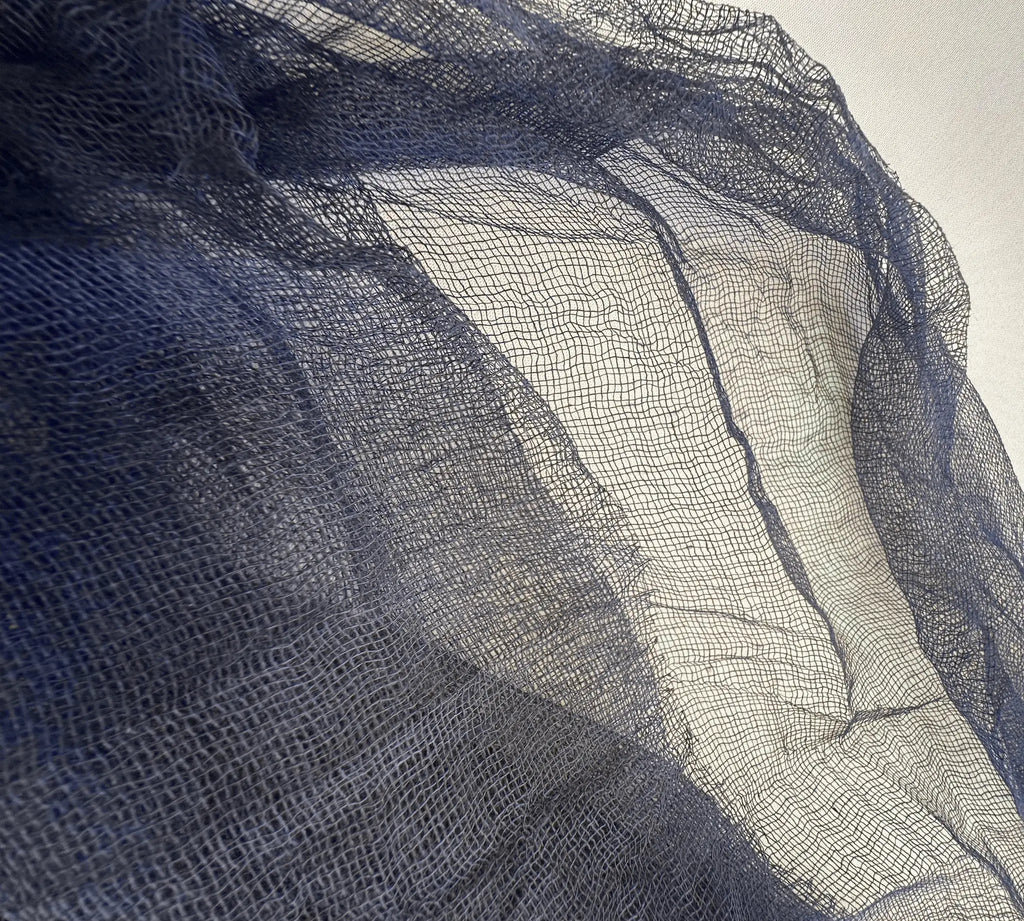 A close-up of sheer dark navy blue mesh fabric draped diagonally across the frame, showing its fine woven texture and semi-transparent quality.