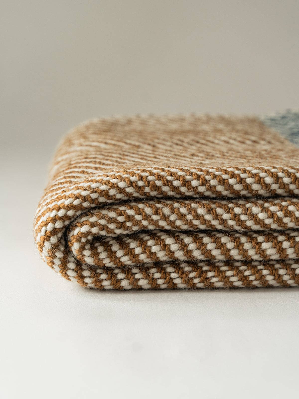 A folded woven blanket or throw in a brown and cream herringbone pattern, photographed on a clean light background.