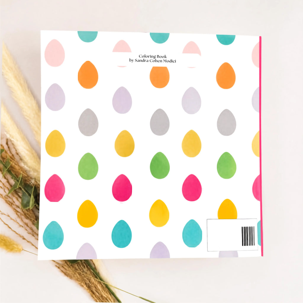 A coloring book author title 'Coloring Book by Sandra Colom-Medici' featuring a white cover decorated with a pattern of colorful teardrop shapes in pink, orange, yellow, green, gray, and teal. The book is styled flat-lay with dried pampas grass on the left side.