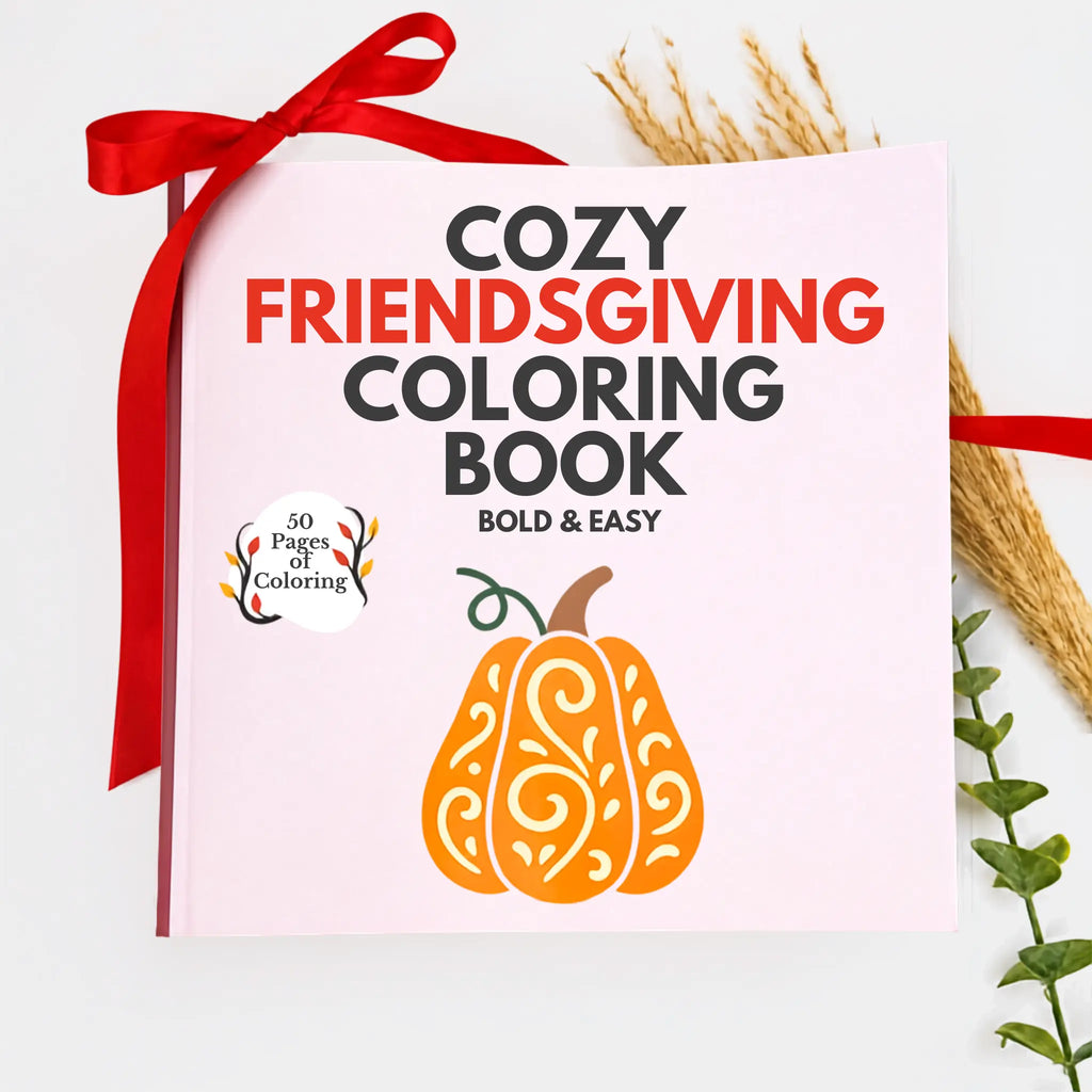 A cozy Friendsgiving coloring book with a light pink cover, styled with a red ribbon and autumn-themed props on a white background.