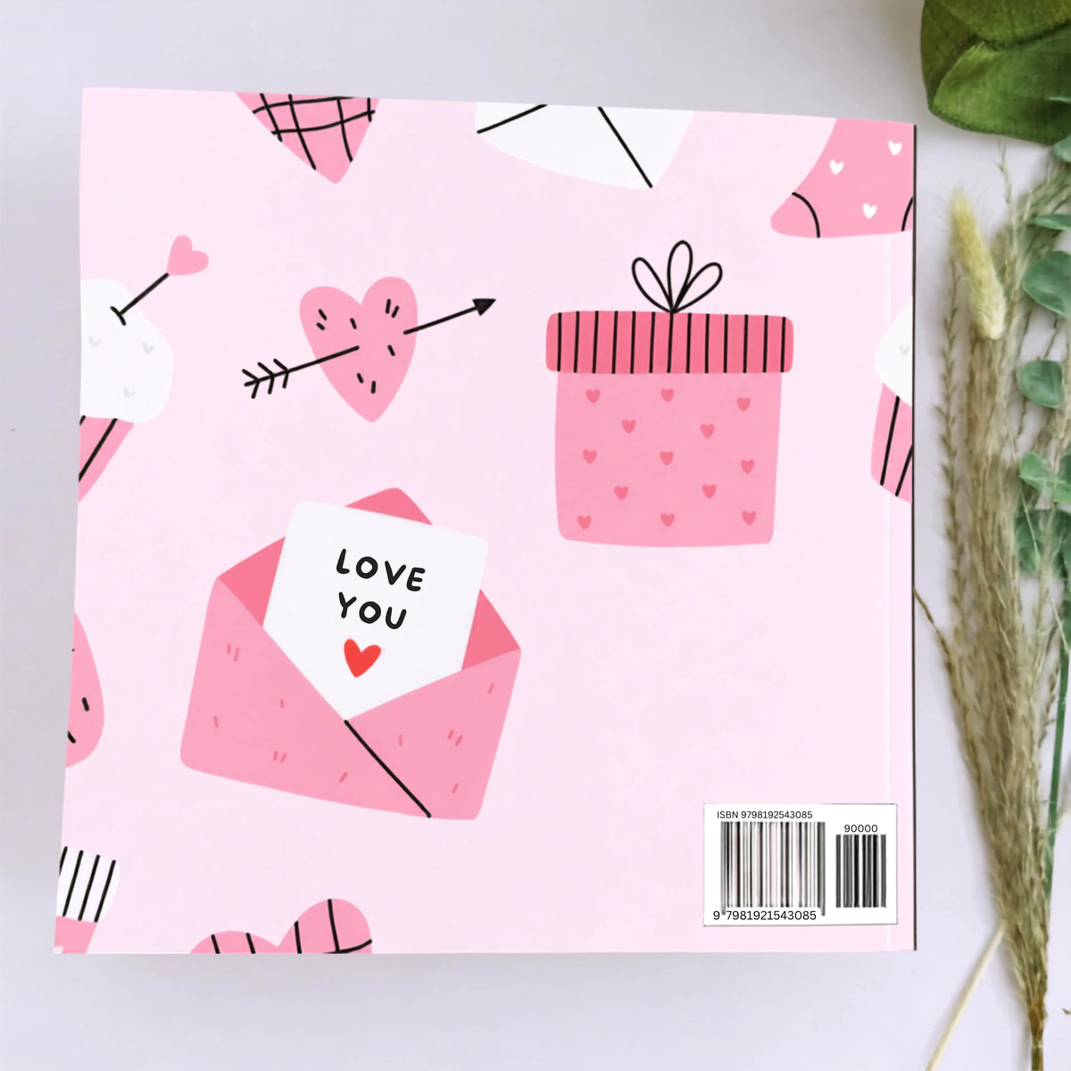 A square pink item with a Valentine's Day illustration pattern, featuring a gift box, heart, envelope, and a card that says 'LOVE YOU'. A barcode label is visible in the bottom right corner.