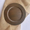 A round dark brown wooden charger plate with a raised rim, shown from above on a beige burlap fabric background.