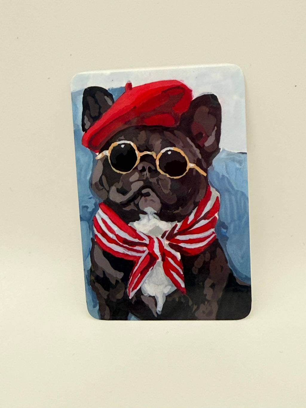 A rectangular art print or card featuring a painted black French bulldog wearing a red beret, round gold-rimmed sunglasses, and a red-and-white striped bow tie, shown against a plain light beige background.
