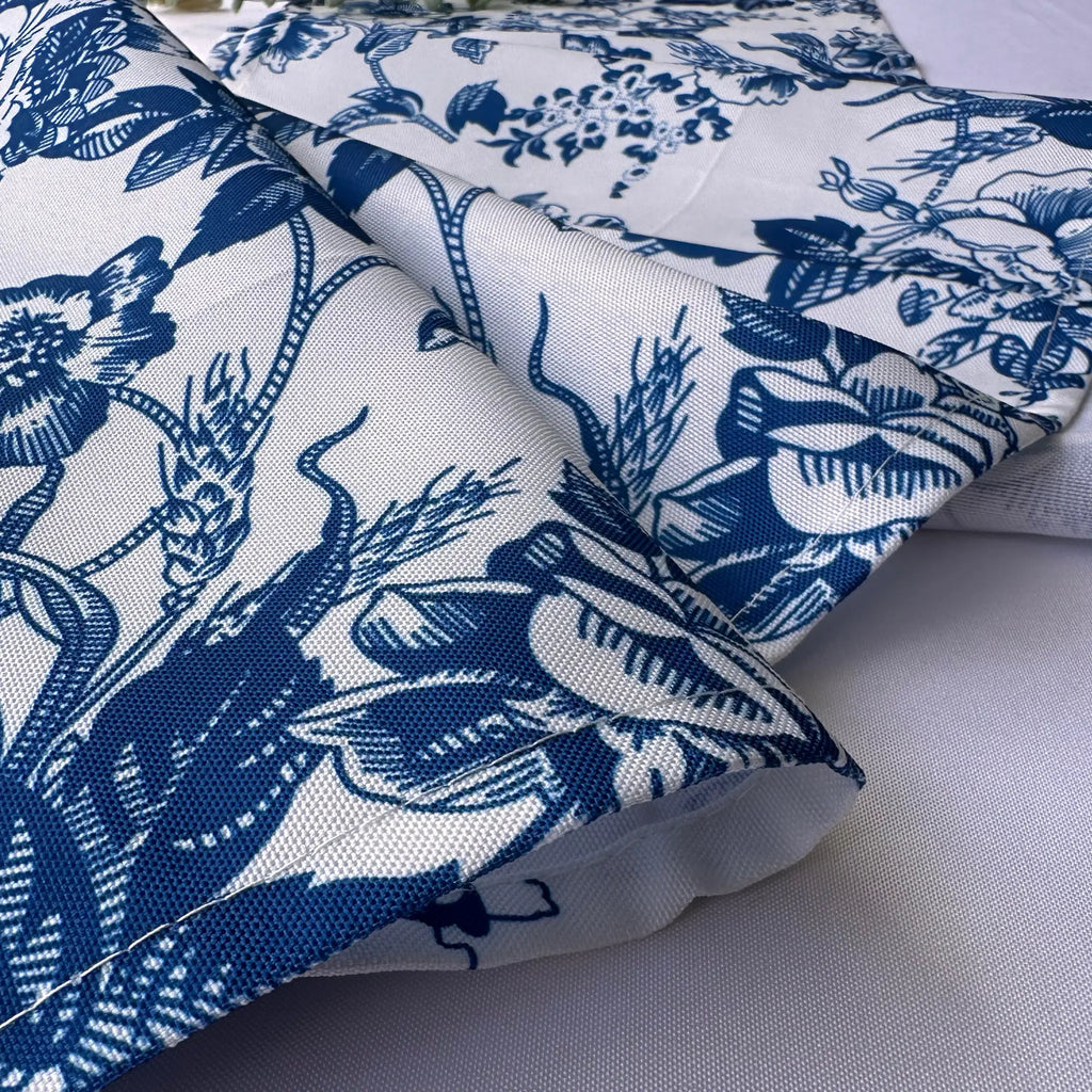 A close-up of folded fabric with a blue floral and botanical toile-style print on a white base, laid on a light neutral surface.
