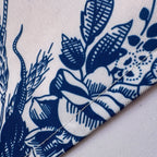 Close-up of a folded textile corner showing a navy blue floral and botanical print on a white fabric background.