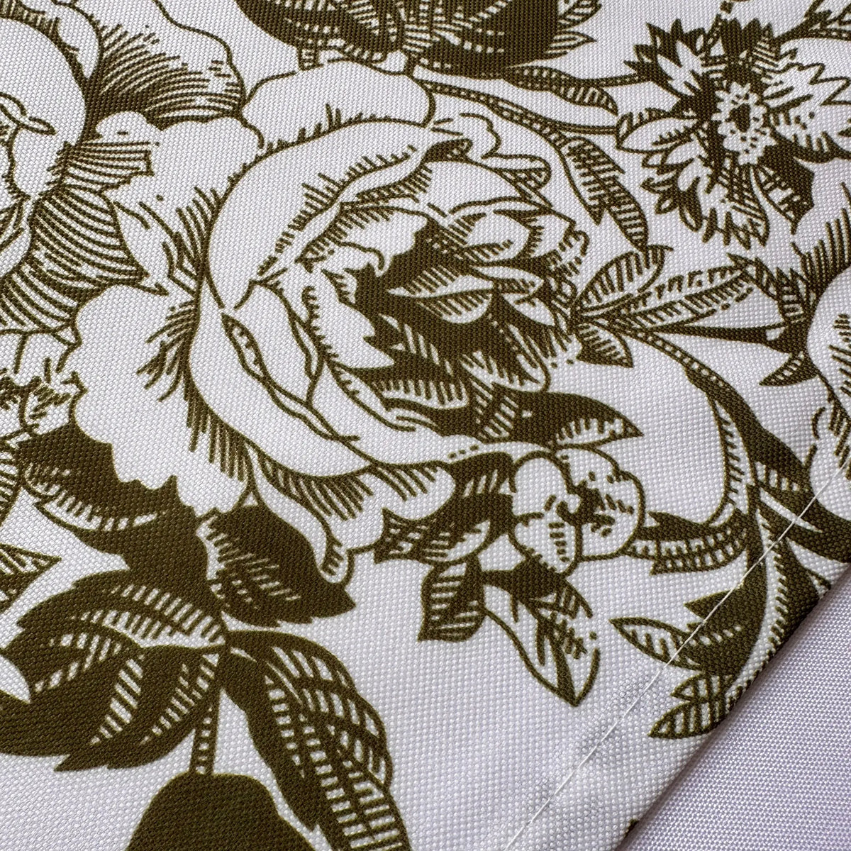 A close-up of a woven fabric with a dark olive-green floral toile pattern on a white background, showing the texture and a folded corner.
