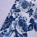 A close-up of a white fabric with a dark blue floral toile pattern, showing the woven texture and a folded seam.
