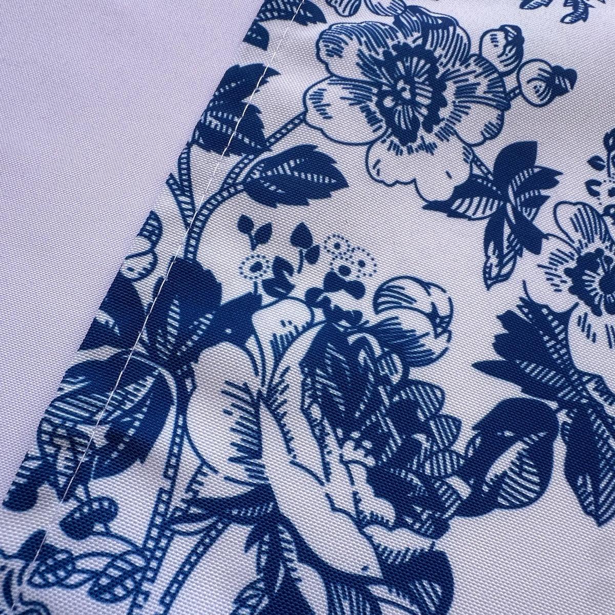 A close-up of a white fabric with a dark blue floral toile pattern, showing the woven texture and a folded seam.