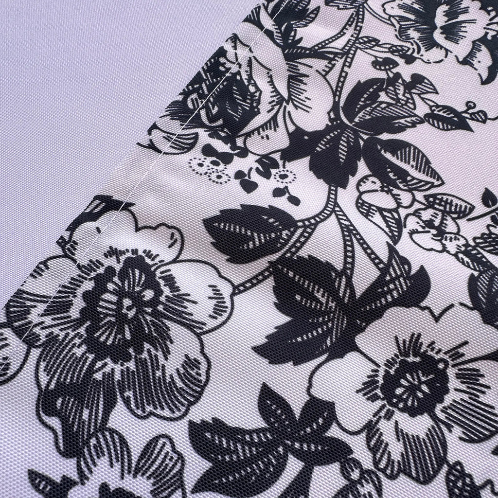 A close-up of a white fabric with a black floral and leaf pattern, laid diagonally across a light gray background.