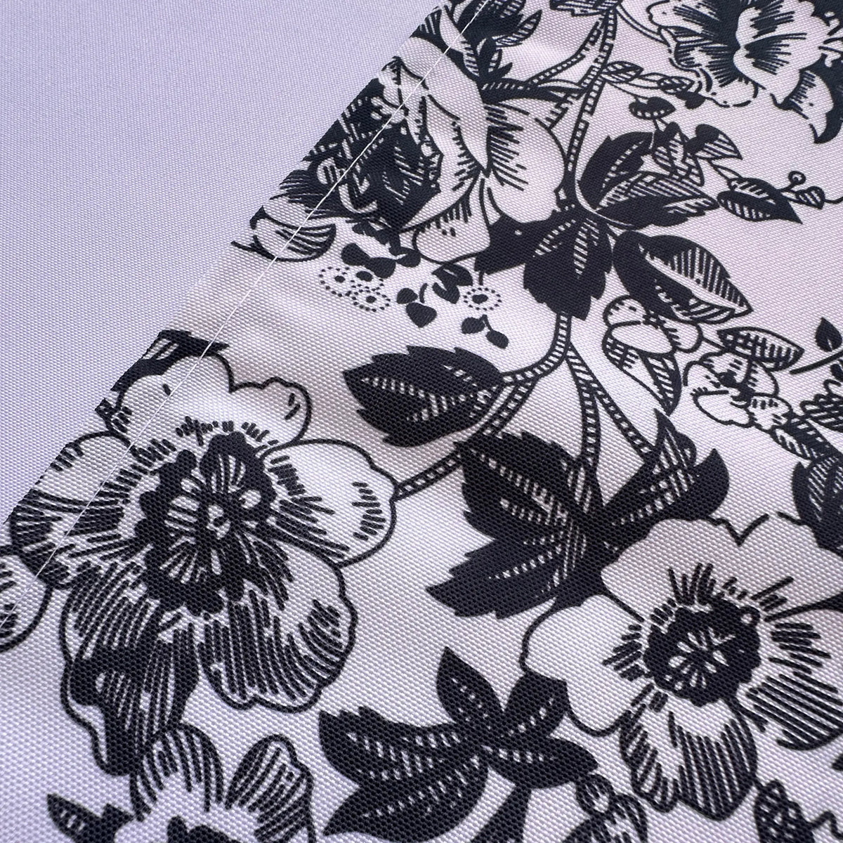 A close-up of a white fabric with a black floral and leaf pattern, laid diagonally across a light gray background.
