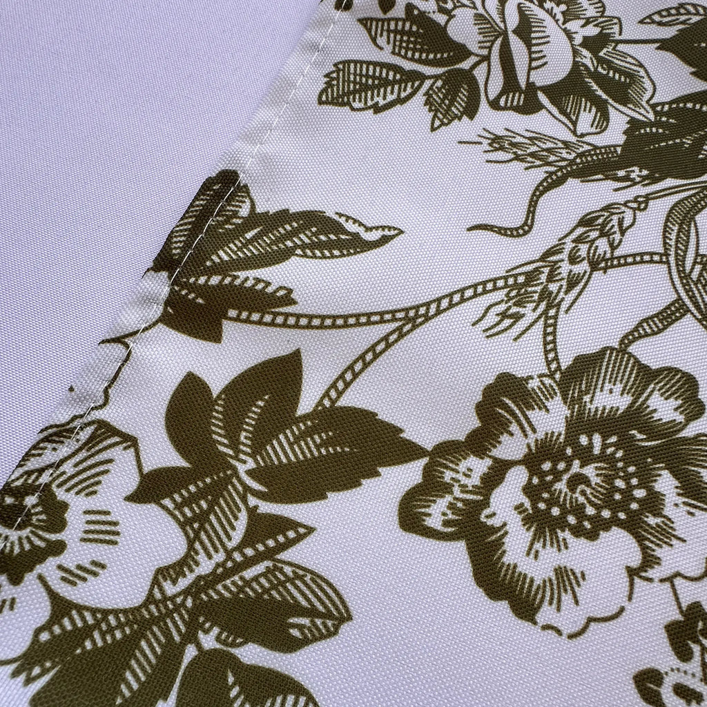 A close-up of a white fabric with an olive green floral toile pattern, showing the texture of the material and the stitched edge.