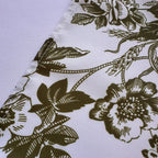 A close-up of a white fabric with an olive green floral toile pattern, showing the texture of the material and the stitched edge.
