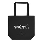 Black tote back with text "merci" in white font and underneath text "The Friendsgiving Shop" in white 