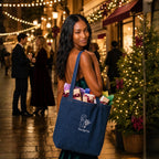 A woman stands on a festive outdoor street at night, carrying a large navy blue denim tote bag filled with wrapped gifts. The bag has a white floral graphic and the word 'Frenchgiving' printed on the front.