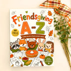 Friendsgiving A-Z Kids Color & Trace Activity Book cover displayed on a light gray surface with a plaid ribbon and dried grasses as styling props.