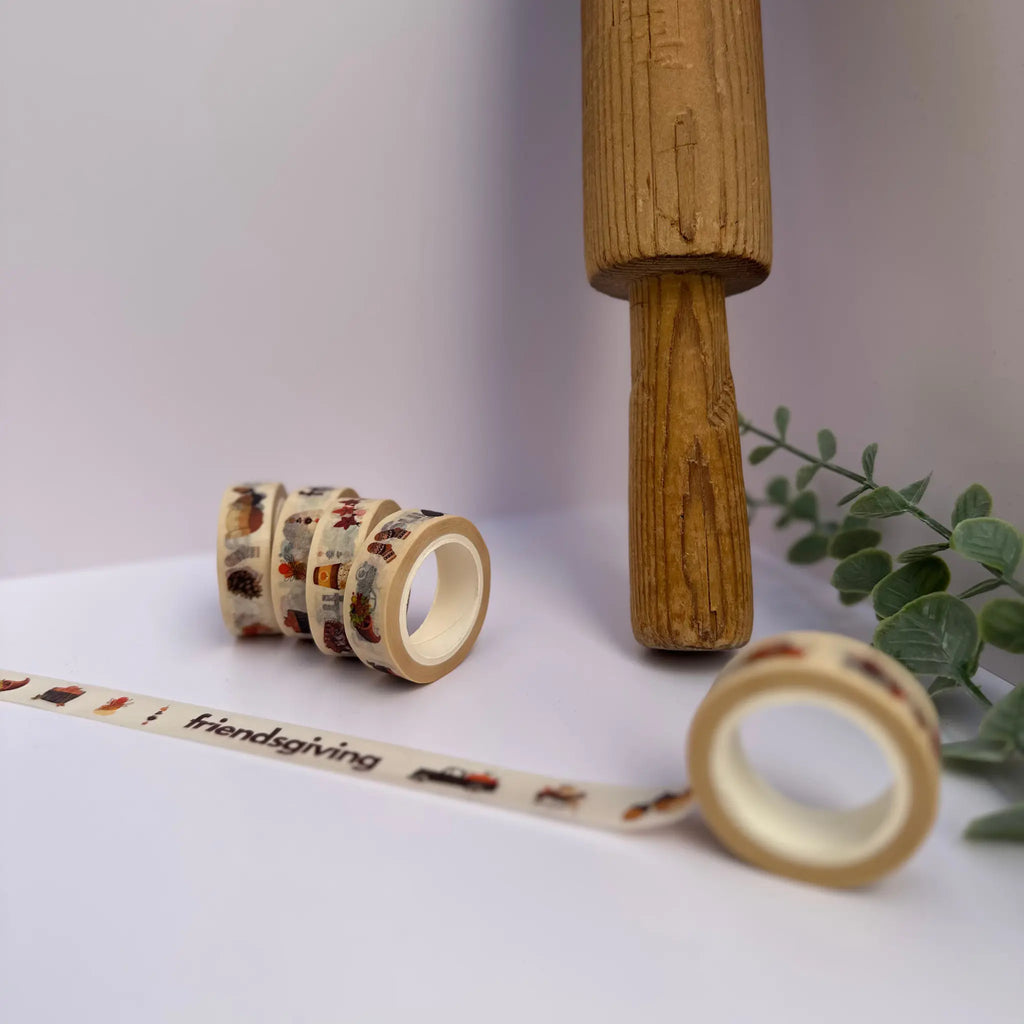 Four rolls of patterned washi tape displayed on a white surface, with one roll unrolled to show the design. The tape features a Friendsgiving holiday theme with illustrations of turkeys, pumpkins, and autumn elements on a cream background.