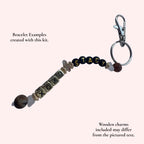 A personalized beaded bracelet keychain with a silver clasp and split ring, featuring wooden letter charms spelling 'STACY' and 'XOXO', on a pale pink background with descriptive text overlays.
