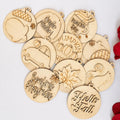 A group of round, light natural wood hanging ornaments with engraved autumn-themed designs and phrases, including acorns, pumpkins, a maple leaf, a squirrel, and seasonal sayings, arranged on a white background with red rose petals at the edge.