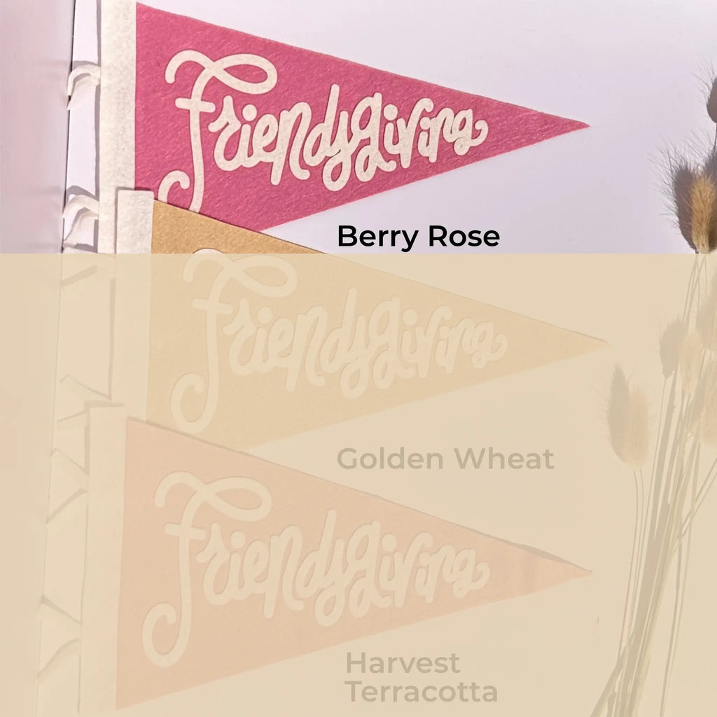 Three triangular fabric pennants with the script word 'Friendsgiving' are shown in different colorways: a pink 'Berry Rose' version, a golden wheat beige version, and a terracotta beige version. The image features a split design with a clear top half and a faded, reflective bottom half.