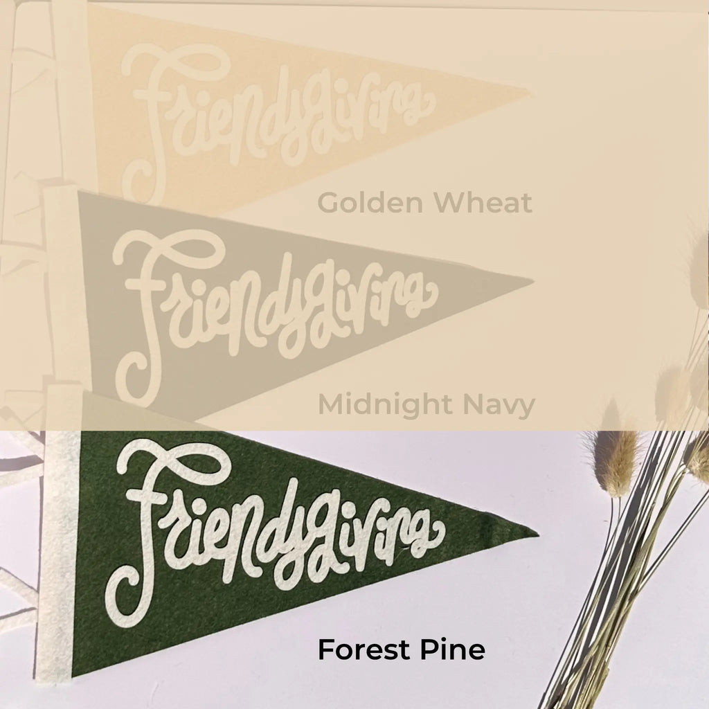 Three triangular pennant flags with the script word 'Friendsgiving' are shown in three colorways: Golden Wheat, Midnight Navy, and Forest Pine. The top two flags are shown faded and overlaid with their color names, while the bottom flag is in full color with the text 'Forest Pine' below it.