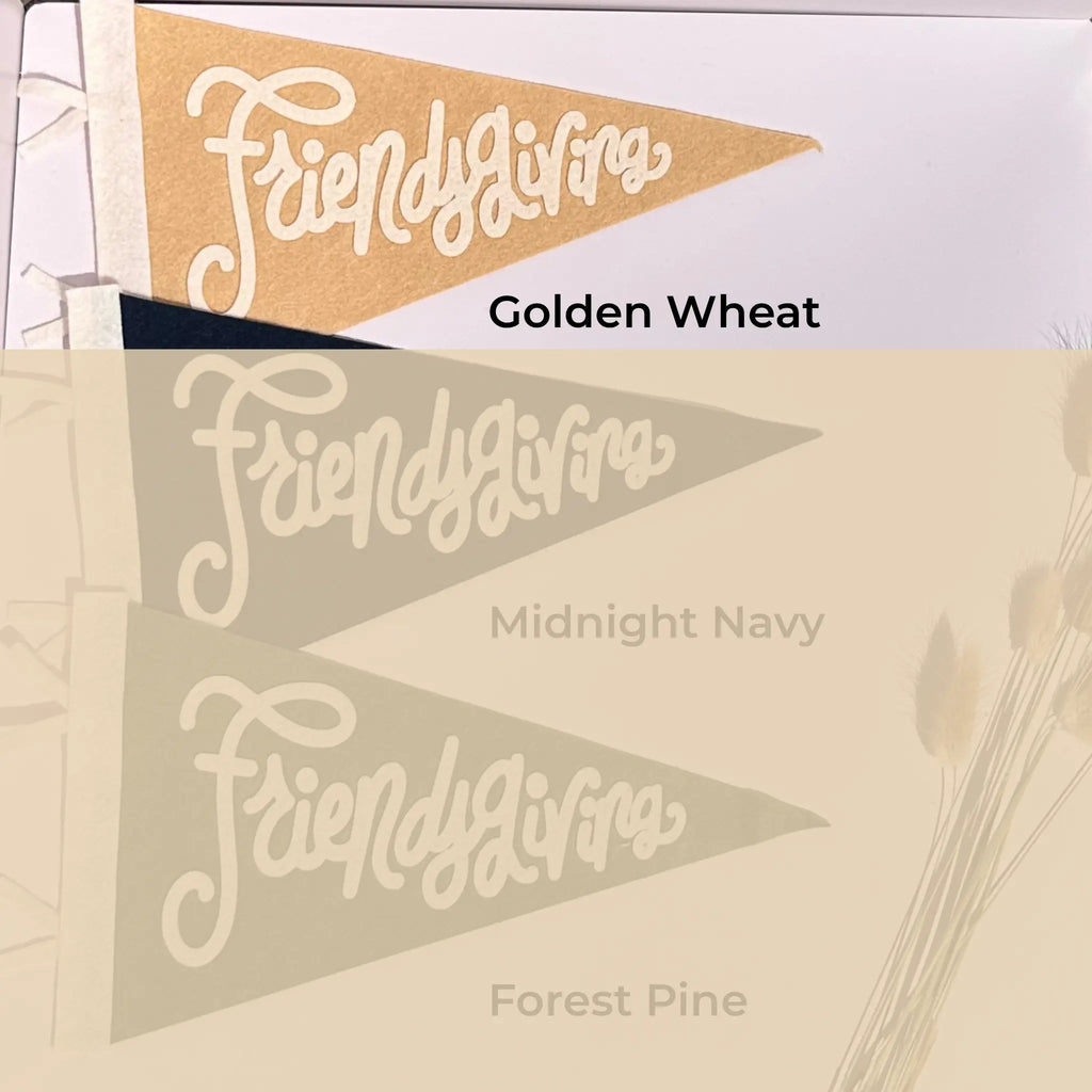 Three triangular pennant flags with the script word 'Friendsgiving' on them, shown in different colorways labeled Golden Wheat, Midnight Navy, and Forest Pine on a light beige background.
