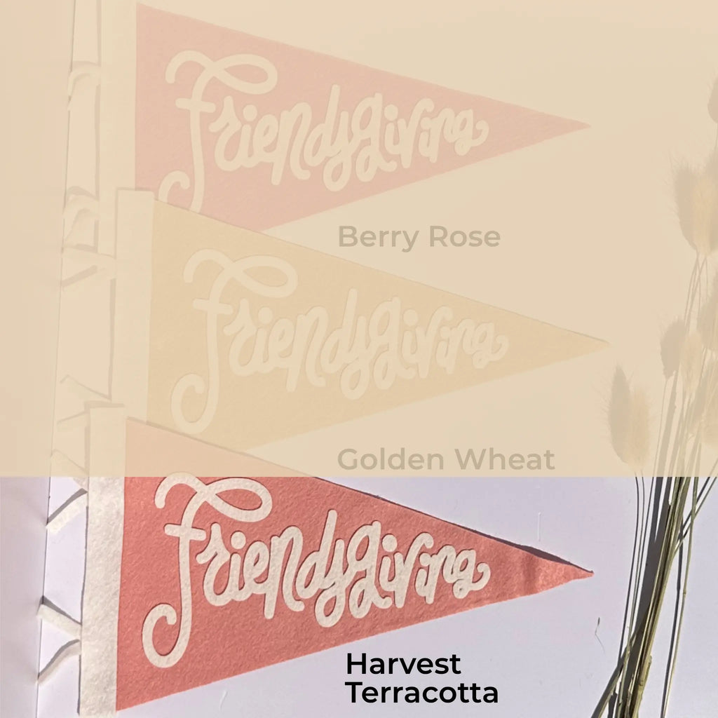 Three triangular pennant flags with the script word 'Friendsgiving' are shown in three colorways labeled Berry Rose, Golden Wheat, and Harvest Terracotta. The top half is a faded beige overlay showing the first two colors, and the bottom half shows the third flag in a styled setting with dried stems on the right.