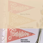 Three triangular pennant flags with the script word 'Friendsgiving' are shown in three colorways labeled Berry Rose, Golden Wheat, and Harvest Terracotta. The top half is a faded beige overlay showing the first two colors, and the bottom half shows the third flag in a styled setting with dried stems on the right.