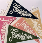 Four triangular felt pennants with white lettering reading 'Friendsgiving' in different colors: navy, pink, peach, and olive green, arranged on a white background.