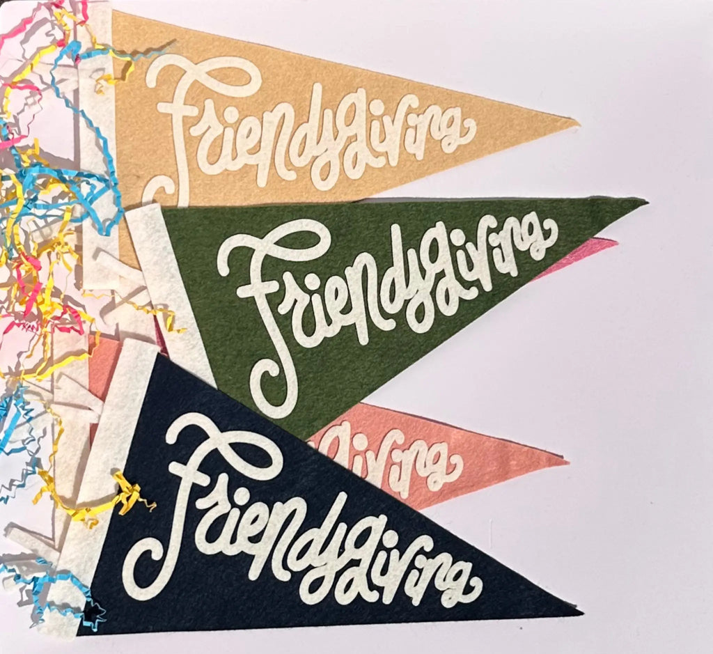 Three triangular pennant flags with the phrase 'Friendsgiving' in white script, shown overlapping on a white background with colorful shredded paper at the left edge.