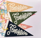 Three triangular pennant flags with the phrase 'Friendsgiving' in white script, shown overlapping on a white background with colorful shredded paper at the left edge.
