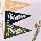 Three triangular pennant flags hang in a row on a white wall. The top pennant is tan, the middle is dark navy, and the bottom is dark green.