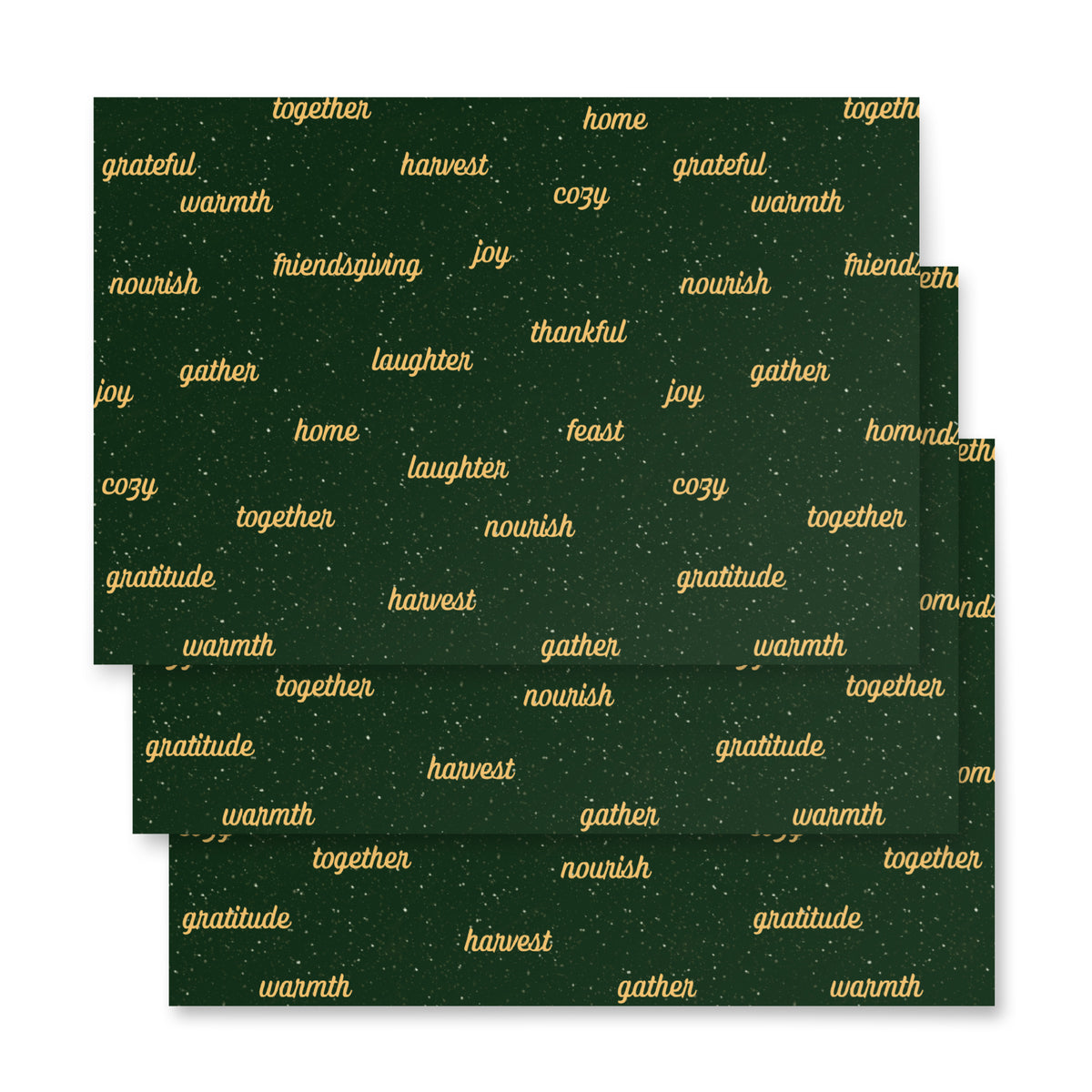 Three square dark green paper sheets of wrapping paper with a repeating pattern of gold words like 'gratitude', 'together', 'harvest', 'home', and 'warmth', arranged in an overlapping stack on a white background.