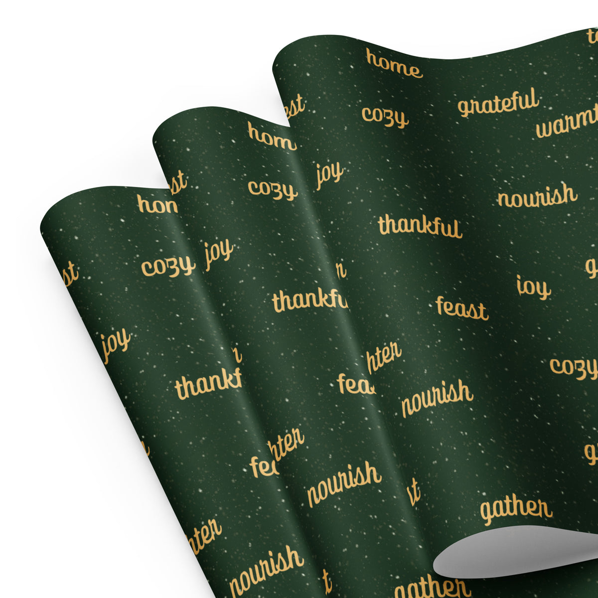 Dark green wrapping paper sheets with a repeating pattern of gold holiday words like 'thankful', 'nourish', 'joy', and 'gather' on a white background.