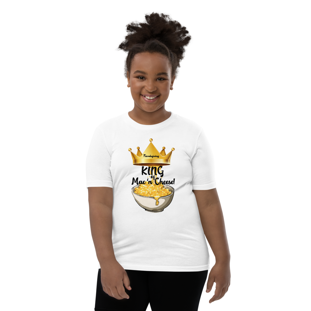 A smiling girl with her hair in a high puff stands against a plain white background wearing a cream-colored t-shirt with a cartoon graphic of a fire element character, paired with black pants.