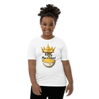A smiling girl with her hair in a high puff stands against a plain white background wearing a cream-colored t-shirt with a cartoon graphic of a fire element character, paired with black pants.