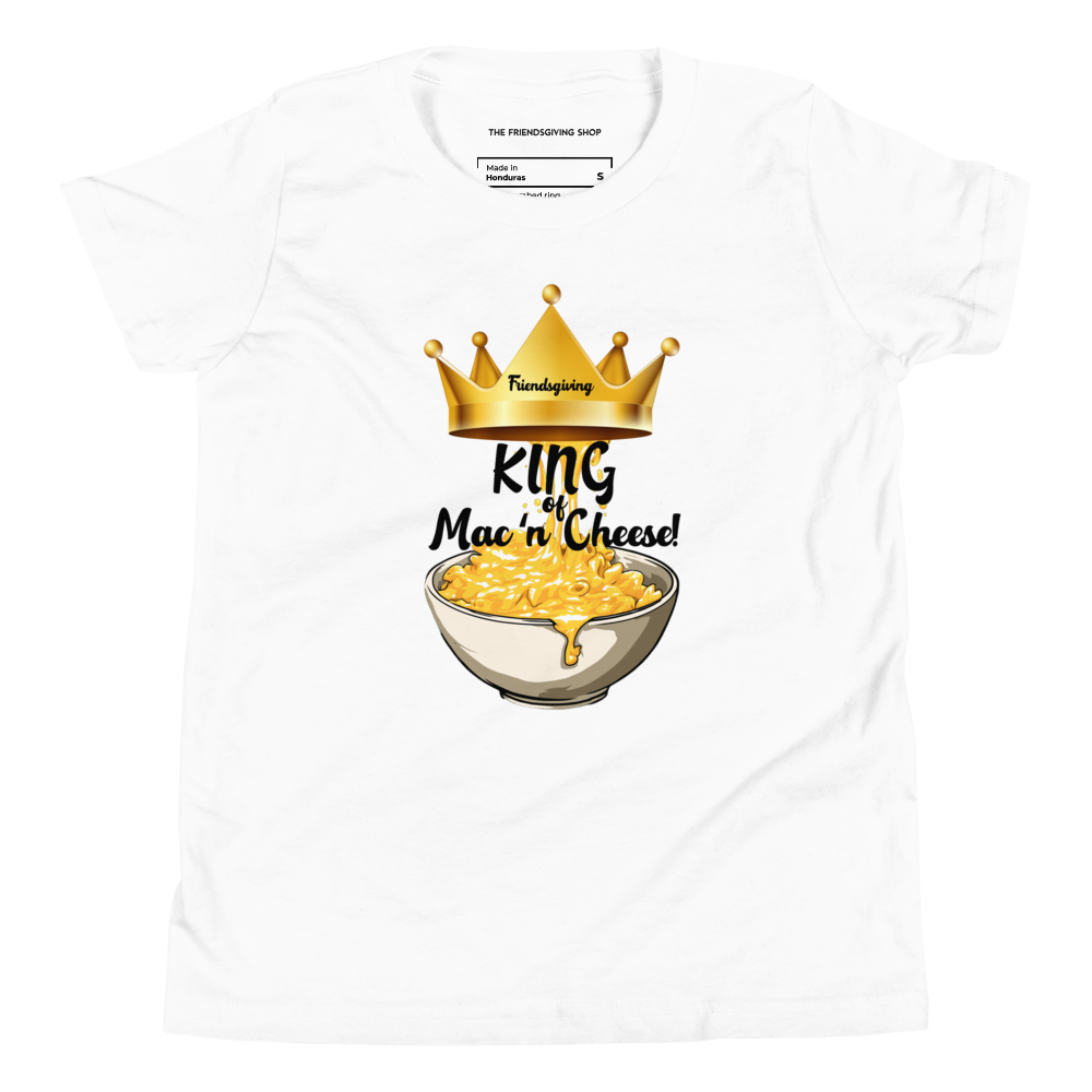 A white short-sleeve crewneck t-shirt featuring a graphic print of a golden crown, a bowl of macaroni cheese, and the text 'King of Mac 'n' Cheese!'. The inner collar shows the brand 'The Friendsgiving Shop'.