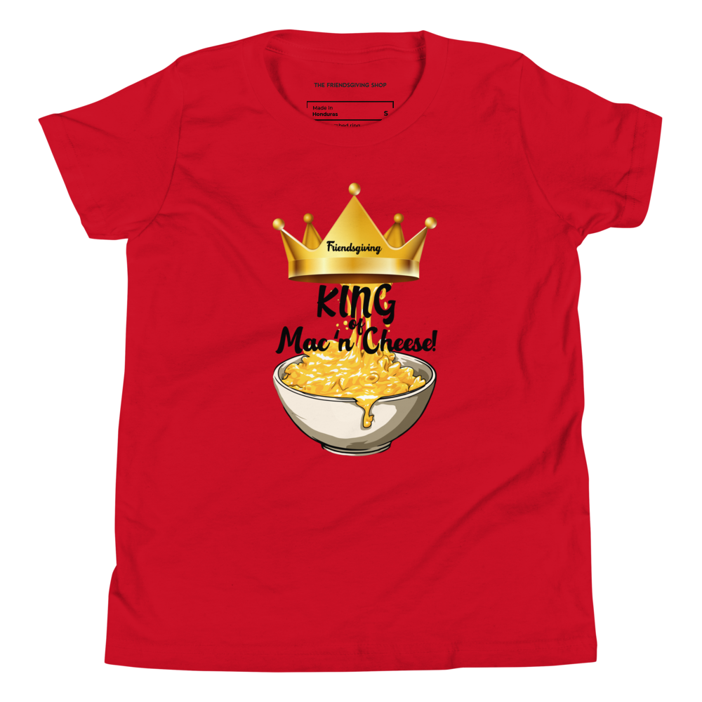 A red short-sleeve t-shirt with a graphic print of a golden crown, the word 'Friendsgiving' in yellow, and the text 'King of Mac n' Cheese!' above an illustration of a bowl of macaroni cheese. The shirt is displayed flat against a solid white background