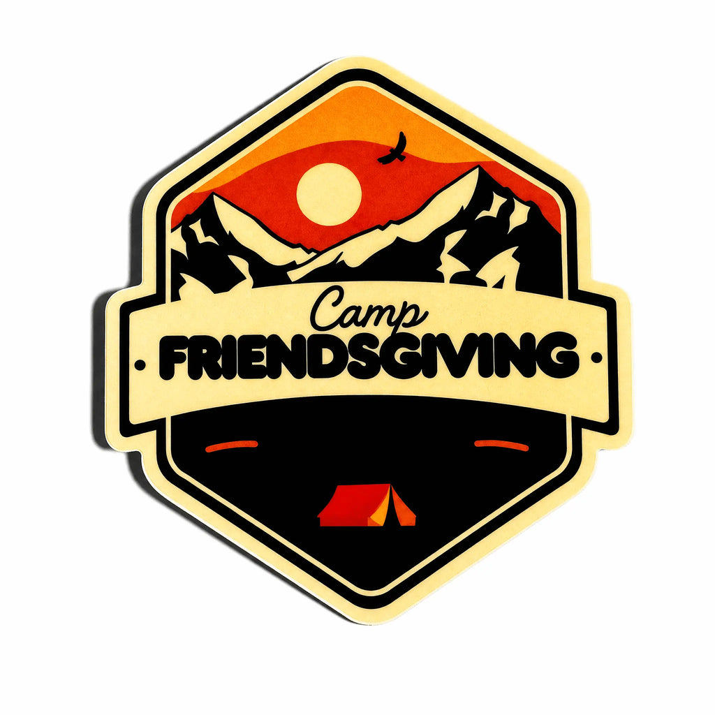 A hexagonal sticker or patch design featuring a mountain landscape with a red and orange sunset, black peaks, a white sun, a bird silhouette, and a cream banner reading 'Camp FRIENDSGIVING' across the center. A small red tent appears at the bottom.